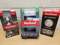 Photo of three packaged door hardware items: two keyed entry door knobs and one deadbolt by Kwikset.