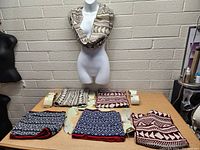 Mannequin displaying one infinity scarf with cream and brown geometric pattern around neck; five scarves laid flat on table showing various color and pattern options.