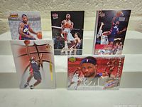 Five LeBron James basketball cards displayed upright on white surface against grey wall background.