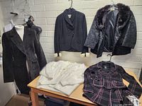 Full view of all clothing items displayed on hangers and a table, showing various jackets and coats including wool, velvet, and fur materials.