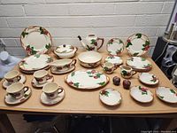 Full table layout showing entire Franciscan apple pattern dinnerware set including plates, bowls, cup and saucer sets, serving dishes, creamer and sugar, salt and pepper shakers.