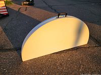 Round folding table in folded closed position showing semi-circle shape and carrying handle on edge.