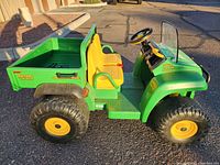 Left side profile of the green ride-on truck showing body, wheels, seating area.