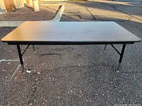 Front view of folding table showing woodgrain top and black metal legs in low height setting.