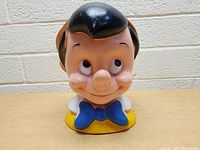 Front view of the Pinocchio coin bank showing the face, hair, bow tie, and yellow collar.