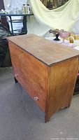 Side view of vintage wooden storage chest showing wood grain, glass knobs, and scratches.