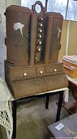 Full front view of rusted cast iron cabinet with dual top cylinders, central porcelain knob column, three drawers, and roll-front compartment