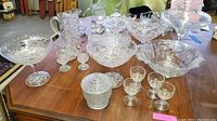 View of entire collection on wooden table, showing bowls, pitchers, stemware, vases, and covered glass items with cut glass patterns