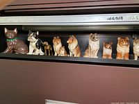 Photo showing nine ceramic animal figurines including a brown cat with green collar, Boston Terrier, and multiple collie dog figurines arranged in a row on a shelf.