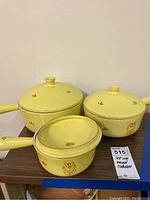 Three yellow cast iron enamel pots with lids decorated with brown floral patterns, sitting on a wooden table.