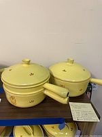 Side view of the yellow enamel double boiler and pot with lids, showing floral design and handles.