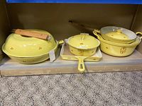 Photo showing the full set of five pieces: covered skillet/fry pan with wooden handle, covered pot, small lidded saucepan/skillet, baking tray, and ladle