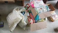 Three containers including two large bags and a cardboard box filled with assorted fabrics and sewing patterns.