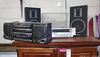 Toshiba receiver with two speakers on a wooden cabinet with a Sharp boombox next to it, showing overall condition and setup