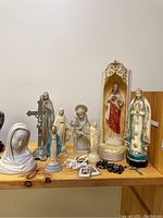 Group of religious figurines including Jesus, Mary, saints, and rosary beads on a wood surface