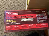 Photo of the Craftsman Chain Drive Garage Door Opener System box showing brand, model number 953975, and features such as anti-burglary coding, automatic safety reverse, emergency manual release, strong reliable drive, and two lights.