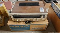 Front view of Nikko 5055 stereo receiver resting on its original branded box, showing the wood top, metallic front panel, and multiple control knobs including tuning dial.