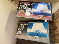 Two boxes of solid brass candelabra table lamps stacked to show front labels and images of the lamps.