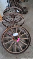 Two wagon wheels placed on concrete floor: one wooden with metal hub, one iron, both showing weathering.