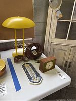 Photo showing the yellow desk lamp, brown retro phone, Seth Thomas clock, and ceramic thermometer on table