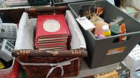 Wicker style basket bin containing stacked red 4x6 photo albums with circular windows visible and grey plastic bin with assorted candles, bottles, and tea light caps