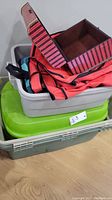 Stack of four bins: three plastic bins in dark grey, green, and light grey; and one red fabric bin with black trim and striped inner lid.