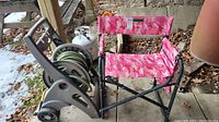 Photo showing the garden hose on the grey plastic reel with wheels next to the pink camouflage lawn chair.