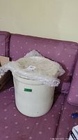 White ceramic crock with bubble wrap-covered lid placed on a purple patterned couch.