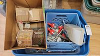Open box showing various items including wooden birdhouses, holiday lights with red bulbs, metal mats