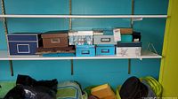 Photo showing various photo storage boxes on a shelf against a turquoise wall, includes navy blue, brown, patterned, and light blue boxes.