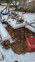 Side view of picnic table with attached benches, metal legs, surrounded by grass and leaves with tool items on top.