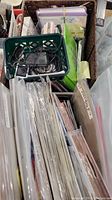 Overhead view showing two baskets filled with scrapbook papers, albums, some plastic sleeves, and accessories. A smaller green basket contains cables and charger.