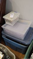 Three stacked plastic storage bins filled with scrapbooking supplies.