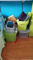 Photo showing assorted plastic storage containers in various colors and sizes stacked near wall and bed.