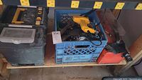 A shelf with two closed storage cases including an orange metal toolbox and a blue milk crate holding assorted tools such as a yellow power drill and a hand saw