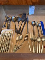 Wide view of all silverware items laid out inside a drawer showing multiple spoons, forks, knives, and serving utensils with visible tarnish.