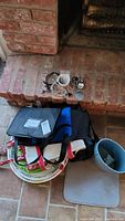 Photo showing black textured book bag, blue bag, hand-painted pottery trays, assorted jewelry including bracelets and pendants on brick hearth with tile floor.