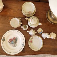 Photo showing the entire set including teapot, sugar bowl, creamer, cups, plates, Peter Rabbit plate, and kissing angel figurines neatly arranged on a wooden surface.