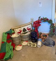 Wide view of tableware and decorations laid out, showing plates, bowls, pillow, jar, wreath, glassware, and holiday fabric items.