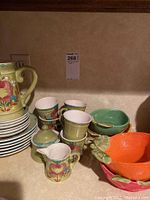 Wide view of ceramic cups, saucers, pitcher, and fruit bowls showing floral and leaf designs.