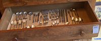 View of a wooden drawer with an assortment of flatware including spoons, forks, and knives neatly arranged.