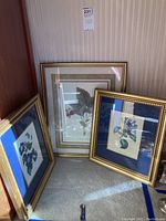Three framed art prints: one larger strawberry botanical print and two smaller floral prints all in gold frames.