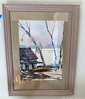 Full view of the framed watercolor painting showing a small house, trees, and lake with muted colors and matting around the print.