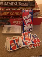 Photo of boxed games stacked: Rummikub, Seinfeld Scene It, Electronic Stratego and Skip-Bo cards with instruction sheet and loose cards.
