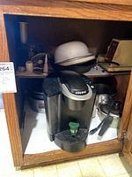 Keurig coffee maker placed inside a wooden cabinet with other kitchen utensils behind it.