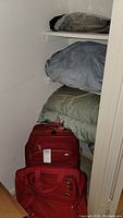 Photo showing two red suitcases and bedding stored on shelves including bed covers and pillows
