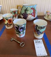 Pitcher and four glasses arranged on wooden surface showing hand-painted fruit designs