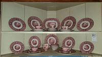 Two shelves displaying stacked Royal Staffordshire Pottery Jenny Lind 1795 dish set items arranged with cups, saucers, plates, and serving platters.