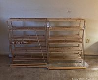 Two lightweight wooden shelving units placed side by side against a wall with tag label on top unit in the center. Shelves are made of slatted wood with vertical metal supports.