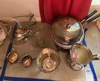 Image showing silver plated fondue pot with lid and black handles, various silver plated bowls, creamer pitcher, and serving spoons arranged on carpet.